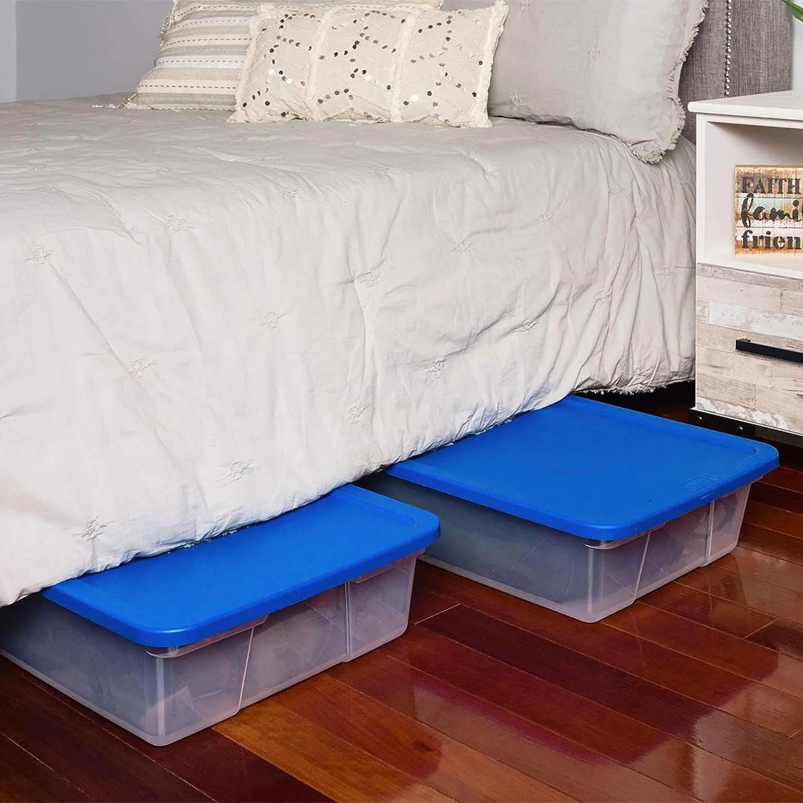 Two HOMZ Snaplock 28-quart bins with blue lids slid under a bed on a wood floor.